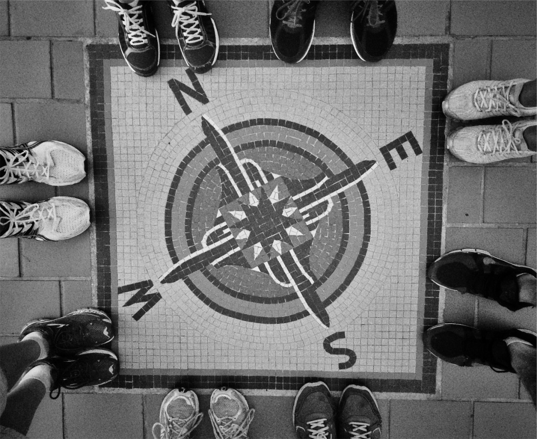 black and white image of a compass painted on the floor with , N, S , E , W with two sets on feet on each one